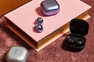 Samsung Galaxy Buds Pro in purple, black, and silver sitting atop a pink book on a rust colored rug.