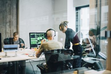 Engineer discussing with colleague while coding over computer at office