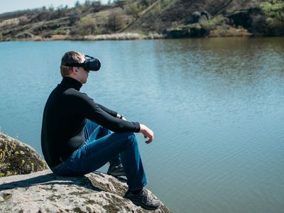 man sitting on a rock near a lake while wearing a VR headset