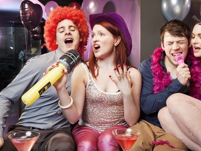 Two couples singing while wearing party props and sitting on a couch.