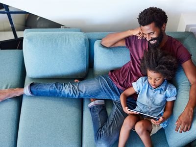 A father and daughter sitting on a couch using a tablet computer