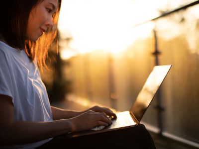 A woman sitting looking at her laptop in subdued lighting outdoors