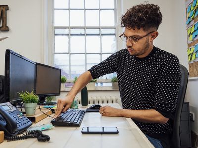 A man sitting at a computer desk and cleaning a black mechanical keyboard.