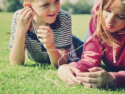 Two children lying on grass listening to music through a smartphone