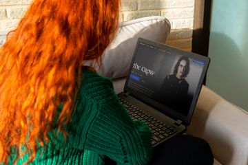 A woman with red hair and a green sweater watching The Crow movie on her laptop.