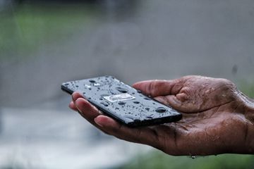 A hand holding a wet smartphone in their palm.